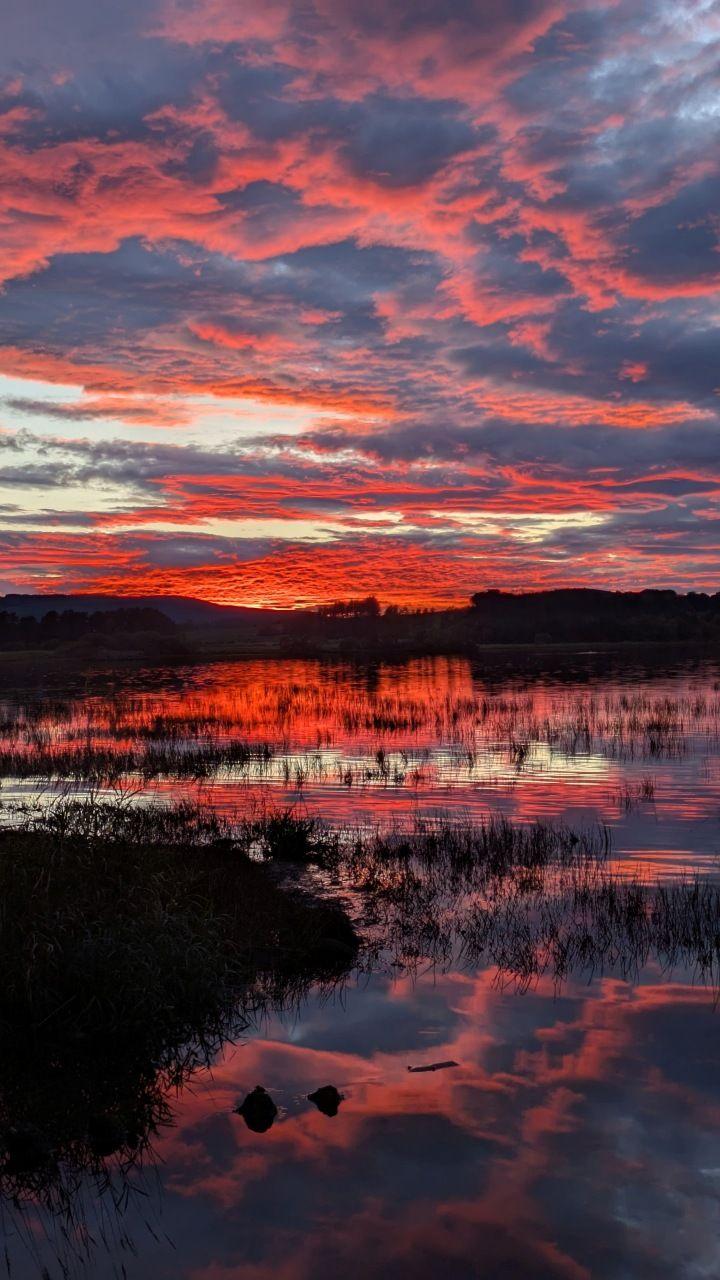 A loch with the sky photographed at sunset, covering the scene with warm red light