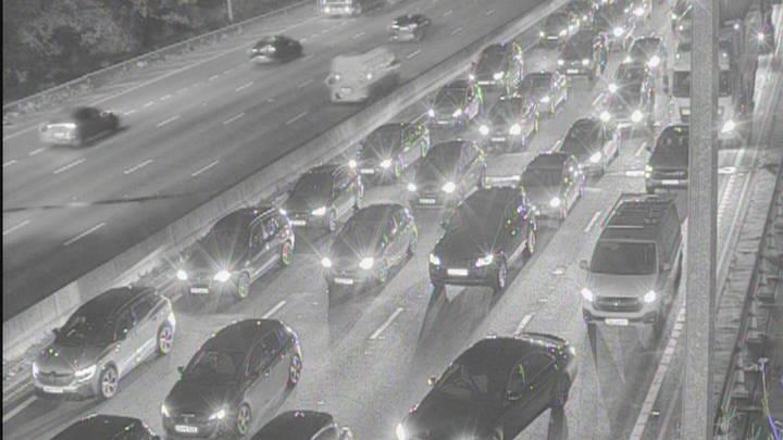 A traffic camera image of the M25 between Essex and Hertfordshire at night time. There are long queues of traffic across four lanes. Vehicles have their headlights on as they queue.