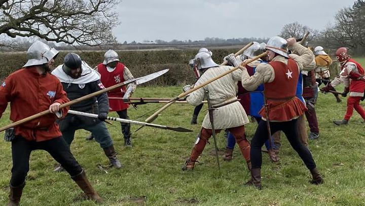 People in medieval garb battling with hand weapons