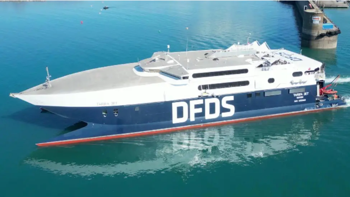 A picture of a large blue body of water with part of the harbour visible. There is a large white and blue boat with DFDS written on its side.