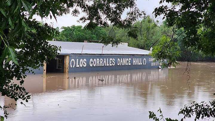 Floodwaters are seen engulfing the Rodeo Los Corrales Dance Hall in Comfort. Trees sit around the hall. 