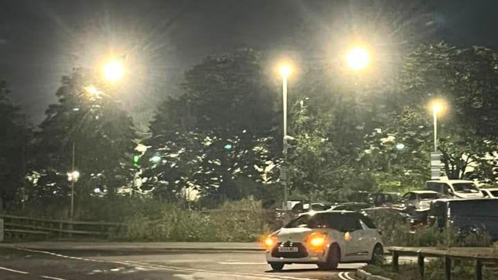 A car pulling out of a junction. It is surrounded by four or five very bright street lights.