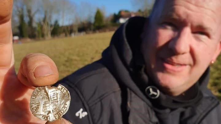 Tommy Coleman stands in a field holding up an old silver coin to the camera.
