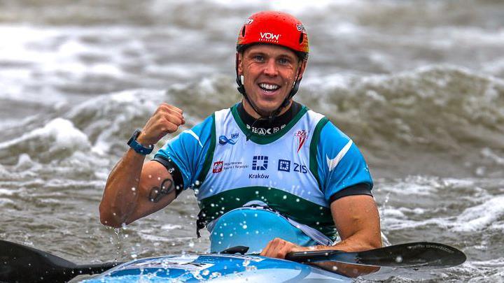 Joe Clarke sits in a kayak and holds up his fist in celebration