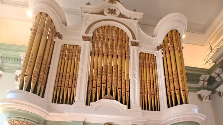 The William Hill organ at Kidderminster Town Hall which has gold pipes and a ornamental white exterior with pale green colouring further down the organ. 