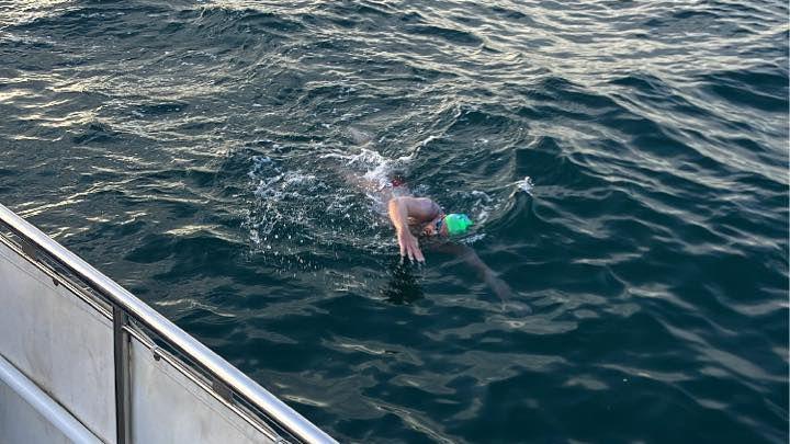 Mr David swimming in the English Channel during the crossing. He is wearing a green swimming hat and is swimming close to a boat.