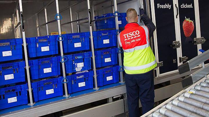 An employee loads crates of produce into a truck before delivery at a Tesco  online distribution centre