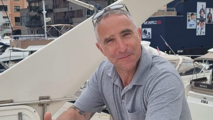 James Kirby smiling, wearing a grey top and sitting on a boat