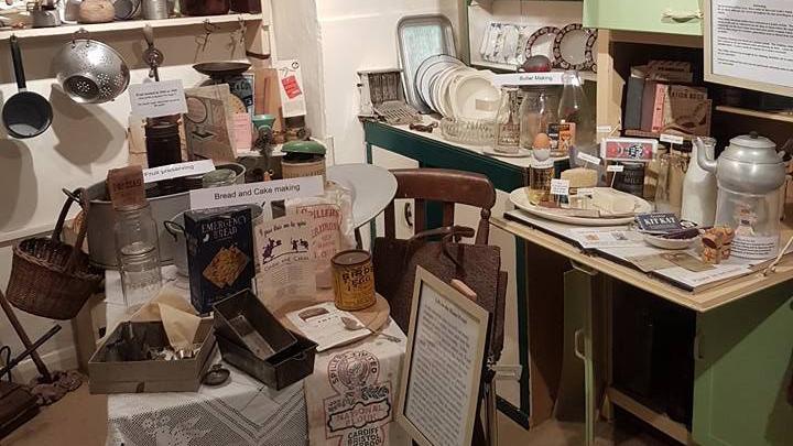 A museum kitchen depicting a kitchen from World War Two. Historical crockery is sitting on tables and kitchen counters, with signs explaining their history.