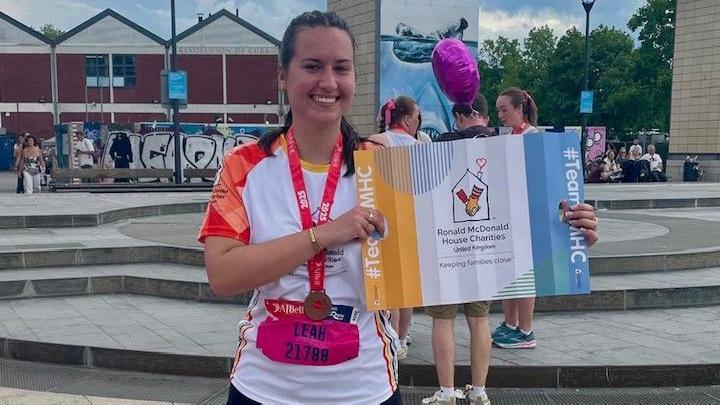 A young women with dark hair poses with her finisher's medal at the end of the Aj Bell Great Bristol Run. She is also holding a certificate