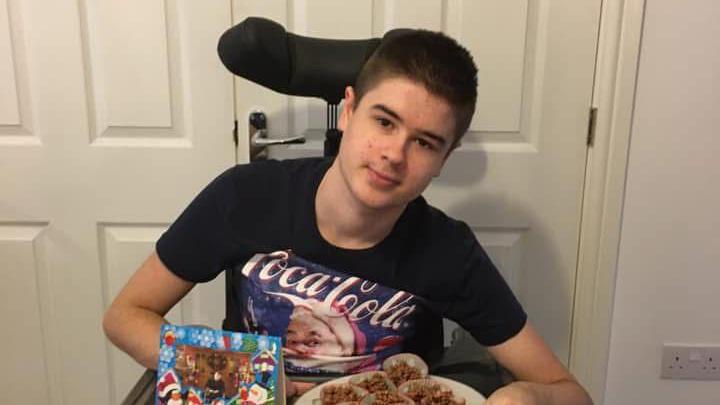 Mr Virgo wearing a black t-shirt sitting in a wheelchair and holding Christmas-themed sweet treats