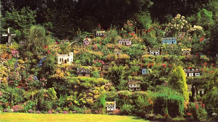 A miniature village on a small slope. There are small houses and plants and a windmill in the far corner. It looks colourful.