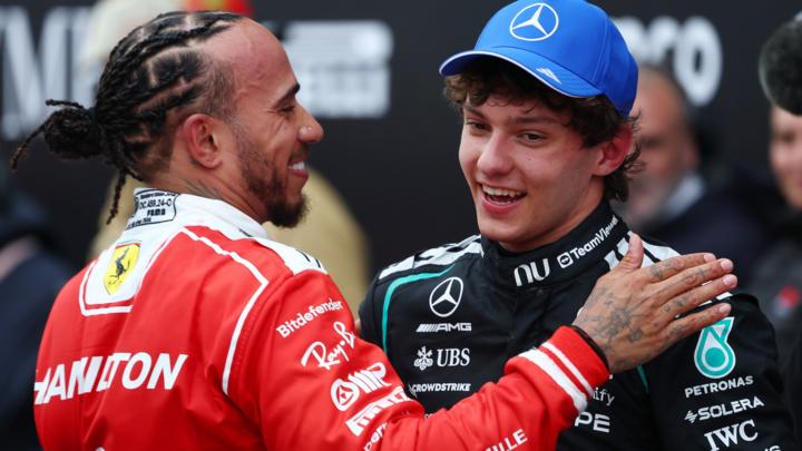 Lewis Hamilton and Kimi Antonelli greet each other after the Canadian Grand Prix, with both smiling, Hamilton in Ferrari's red racing suit and Antonelli in black