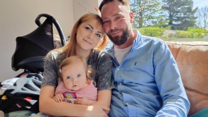 Gary Willard, Daryna Rudomiotova sitting on a couch. Their baby daughter, Emilia, is sitting on Daryna's lap.