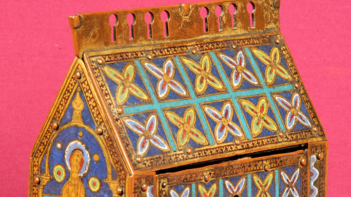 a small box decorated in medieval art with colours of blue, green, red and gold. It has a hand painted illustration of a male saint, st thomas becket 