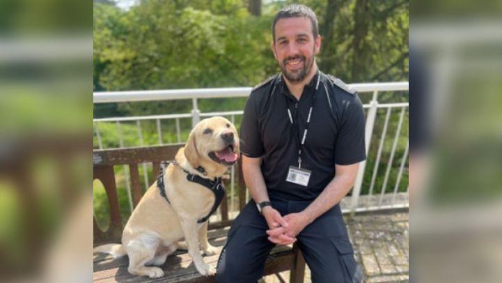 PC Croft sitting on a bench beside a Labrador 