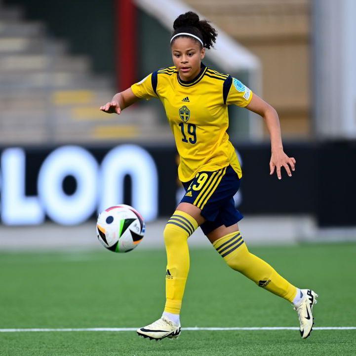 Felicia Schröder playing football. She is wearing a yellow and black Sweden kit with the number 19. She is looking at the ball and controlling it while running.