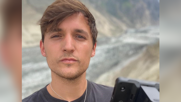 A head and shoulders shot of Nyal, dolding his camera with one hand, with mountain landscape in the background