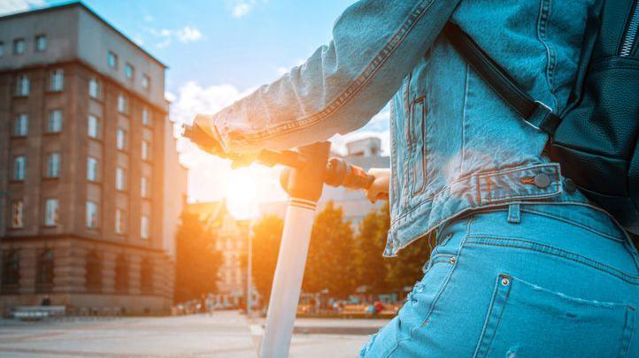 A person on an e-scooter riding in a town, with the sun setting in the background