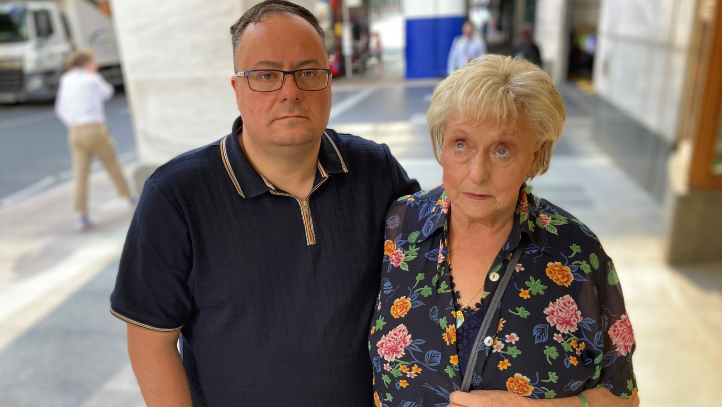 Julie Hogg's son Kevin and mother Ann Ming standing side by side in a street with their arms around each other. Kevin is looking at the camera and Ms Ming is looking upwards. 