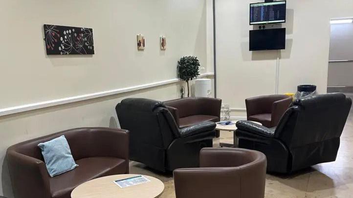 A waiting room with brown couches, tables, black leather recliners and a TV hanging on the wall. 