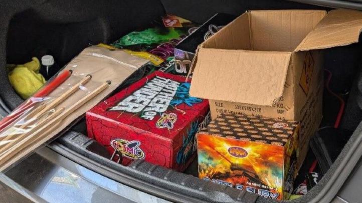 Red, orange, black and brown cardboard boxes containing fireworks in the boot of a vehicle.