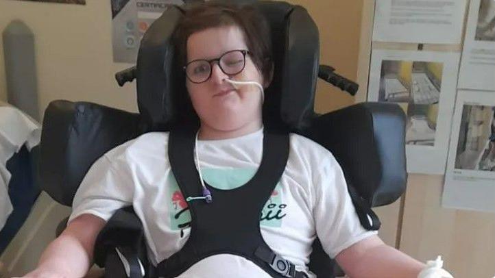 Danny, wearing glasses and a white t-shirt, sits in his specially adapted wheelchair 