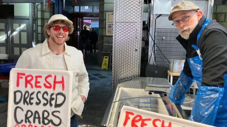 Doncaster musician Adam Taylor in white peaked cap, red sunglasses and white jacket, next to fishmonger wearing a flat cap and blue apron
