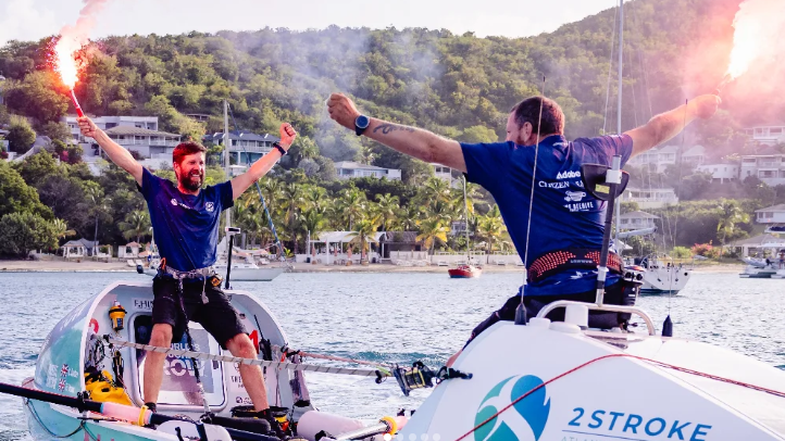 Karl Austen and Ed Shaw wearing navy blue t-shirts and are holding flares whilst standing on there rowing boat.