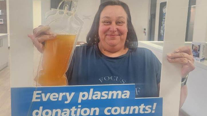 A woman holding up a blood plasma sample and smiling