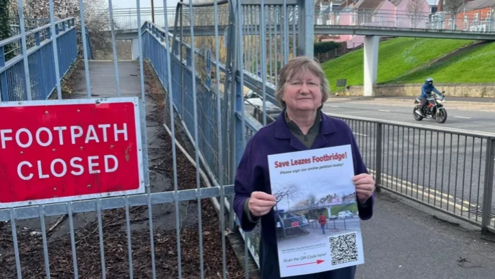 A woman wearing a blue top and short greyish hair is holding a poster saying Save Leazes Footbridge 