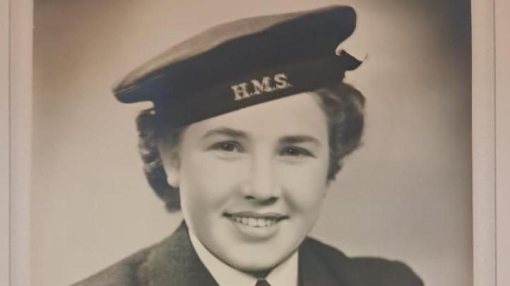 A black and white photo shows a smiling Pat Shepherd in naval uniform with "HMS" on her cap above short, dark hair.