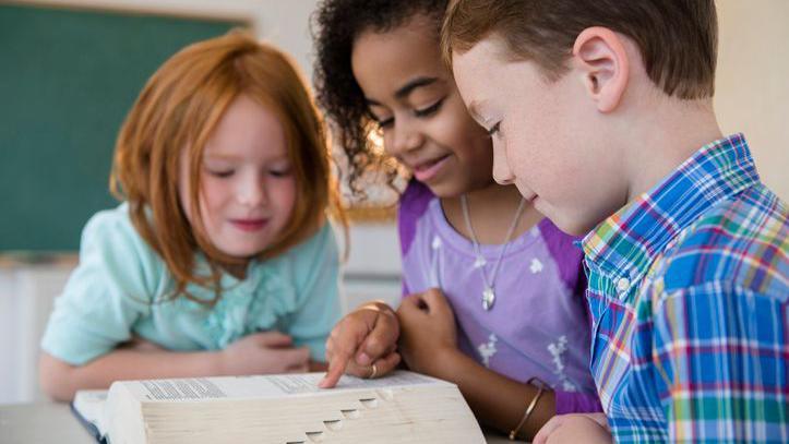Three children looking at a dictionary.