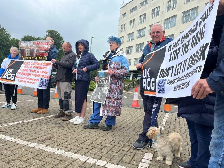 A group of about half a dozen people, standing outside a five-storey building. They are holding banners, one of which says "Stop the Raac - don't let it crack".
