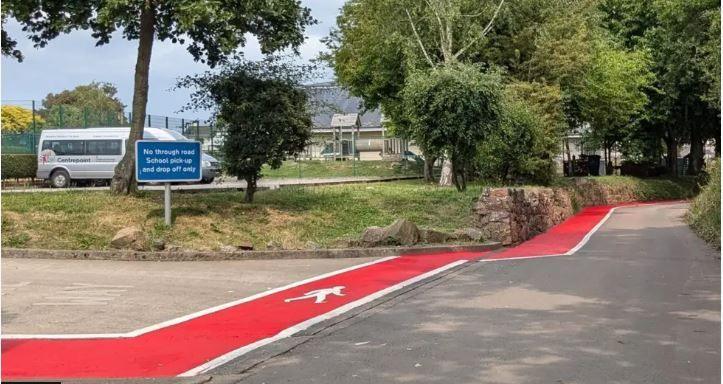 A red stripe with a white border on a lane next to a school