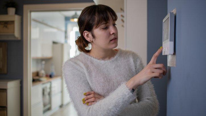 Young woman adjusts the temperature at home with a device on the wall - stock photo