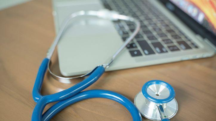 Blue stethoscope and a laptop on a desk. 