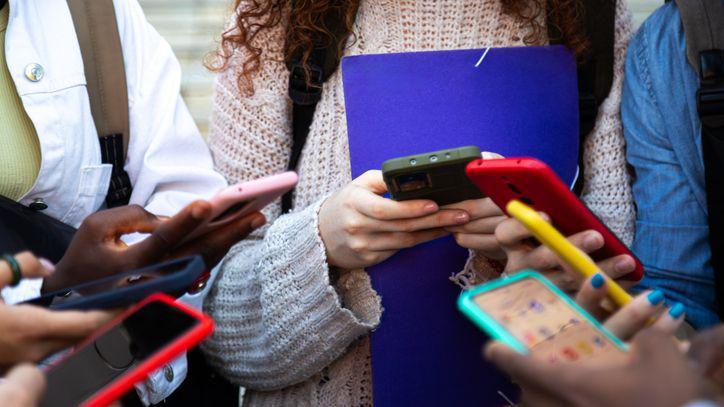 Teenagers in a circle, all holding and using smart phones.