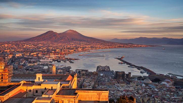 An aerial view of the city of Naples, showing mountains in the background.