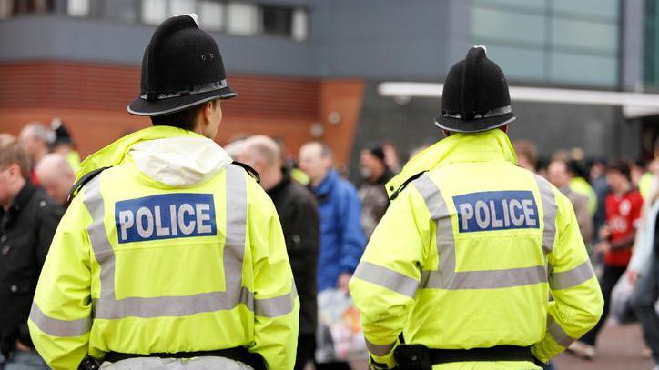 Two police officers in high-visibility jackets looking away from the camera towards a large group of people