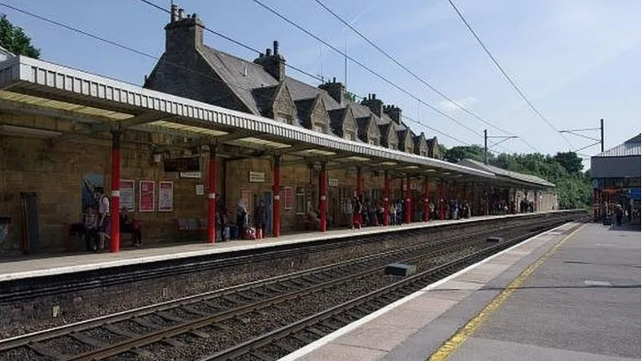 Oxenholme station in the Lake District. It is a Victorian building with a low canopy held up by red pillars and a row of Victorian cottages behind.