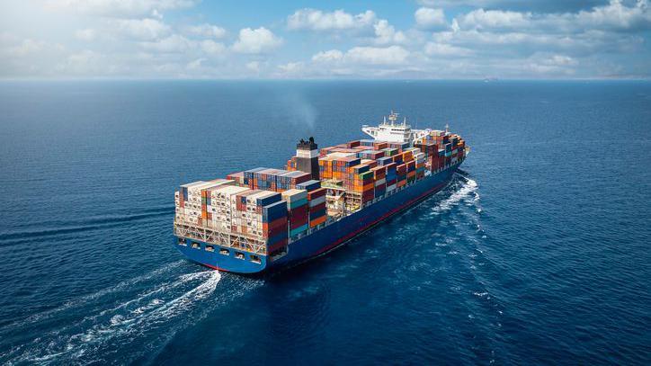 A large container cargo ship travels over calm, blue ocean.