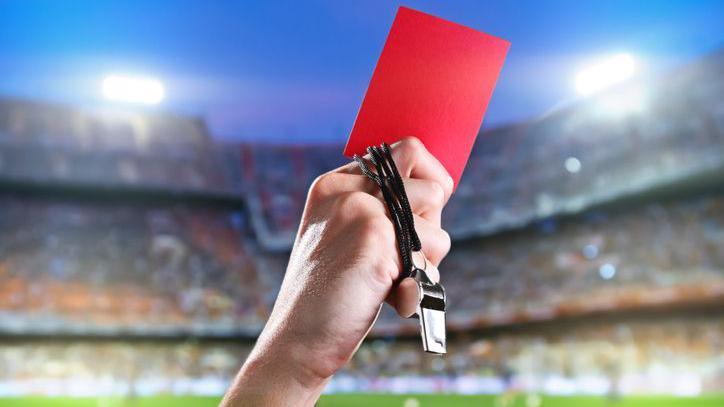 A red card being held up on a football pitch.
