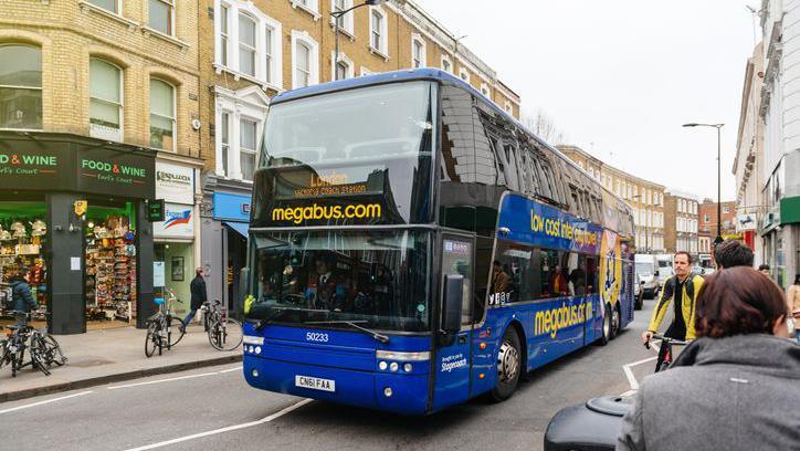 Blue double-decker bus with Megabus livery travelling down a busy street in London