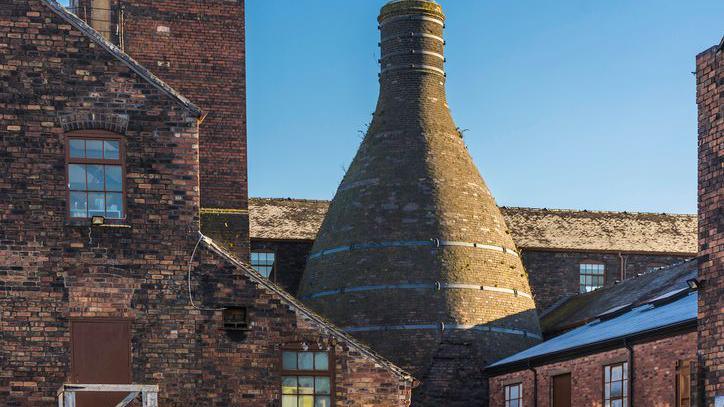 Historic buildings of potteries are located on banks of Trent and Mersey canal in Stoke-on-Trent. Factory and kiln rooftops can be seen.