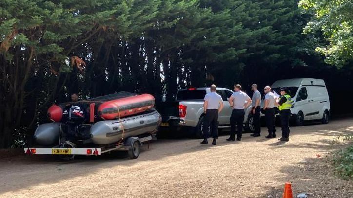 Boats on a trailer at the lake, with police officers standing next to them.