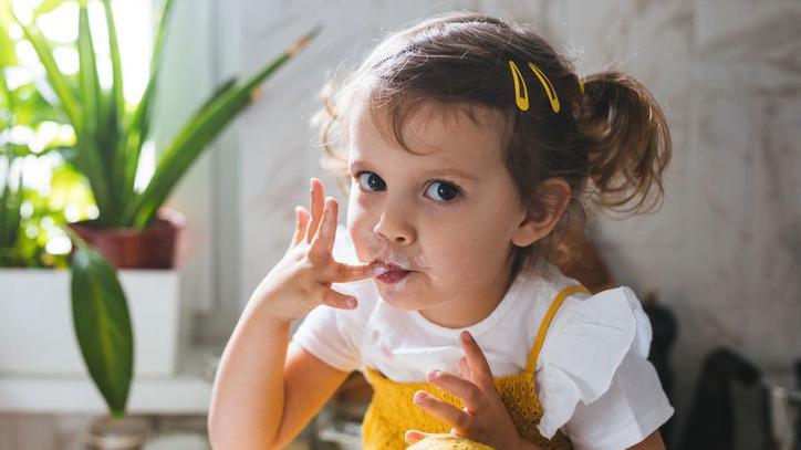 Girl licking her fingers with food on them.