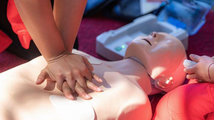 CPR is performed on a dummy. Medical equipment is in the background.