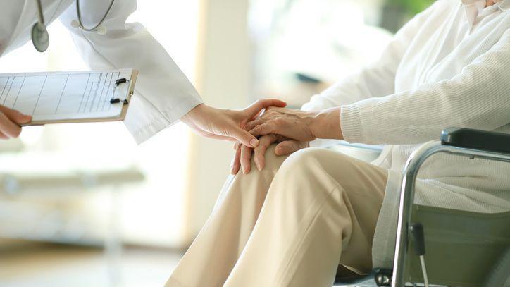 Doctor places hand on the hand of a person in a wheelchair