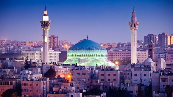 A blue domed mosque dominates a city skyline, with two tall minarets either side of the dome.